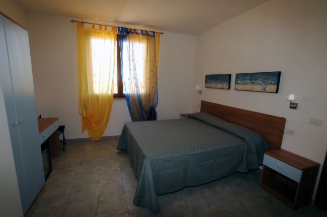 Camera da letto con letto matrimoniale, tende colorate e quadri sul muro.