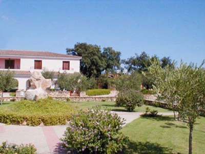 Giardino curato con alberi e un edificio bianco a due piani sullo sfondo.