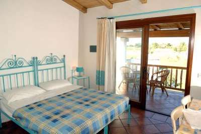Una camera da letto con letto matrimoniale, copriletto a quadri e una terrazza soleggiata con sedie.