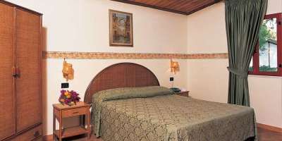 Una camera da letto con un letto matrimoniale, armadio, comodino e tende verdi.