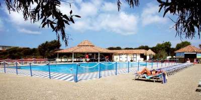 Piscina con sdraio e un grande gazebo in legno, circondata da alberi e cielo blu.