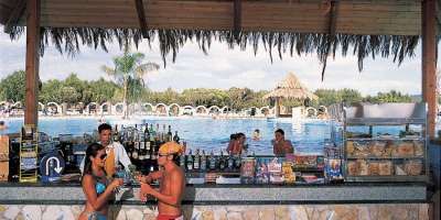 Un bar all'aperto vicino a una piscina, con persone che si godono bevande, palme sullo sfondo.