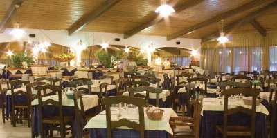 Un ristorante ampio con tavoli apparecchiati, sedie in legno e una luce calda dall'alto.
