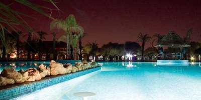 Piscina illuminata di notte tra palme e rocce.