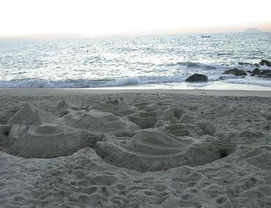 Spiaggia con castelli di sabbia e mare agitato sullo sfondo.
