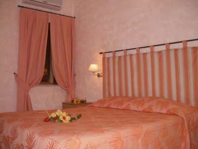 Una camera da letto con pareti rosa, letto matrimoniale con coperta arancione e fiori sul letto.