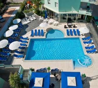 Piscina all'aperto con numerosi lettini e ombrelloni bianchi, circondata da strutture e verde.