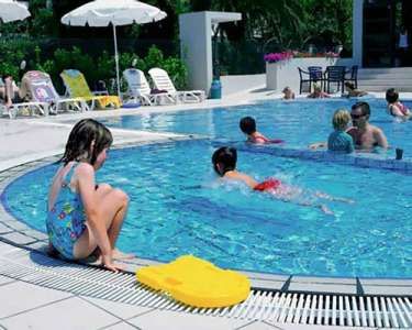 Bambini che giocano in piscina, circondati da sdraio e ombrelloni.