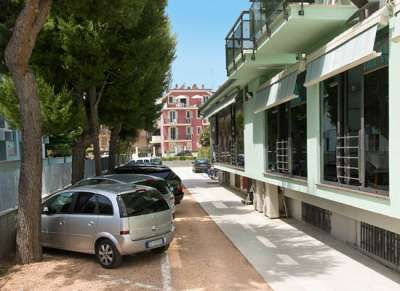 Auto parcheggiate accanto a un edificio verde con vetrate e tende. Alberi sul lato sinistro.