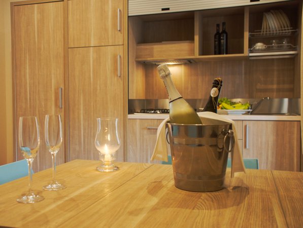 Bottiglia in secchiello su tavolo con bicchieri, cucina in legno sullo sfondo.