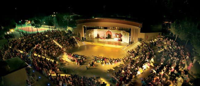 Anfiteatro all'aperto illuminato con pubblico.