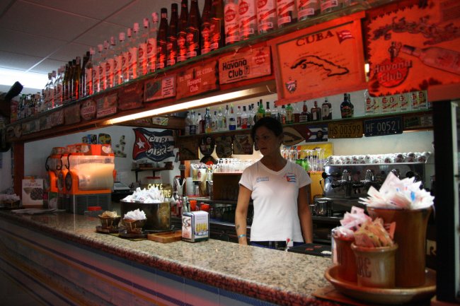 Bar con bottiglie di alcolici e una persona dietro il bancone.