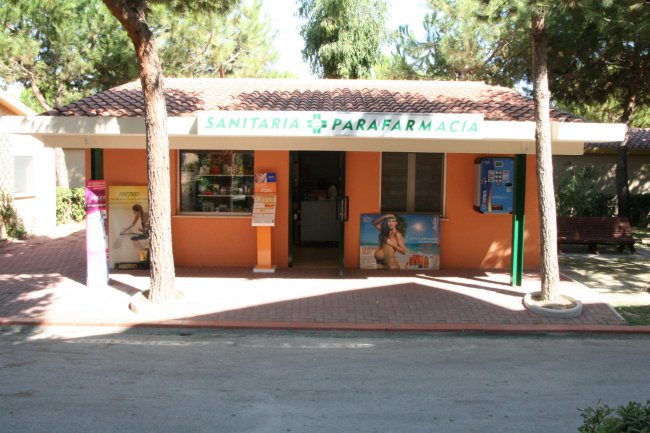 Facciata di una parafarmacia arancione con poster e distributore automatico.