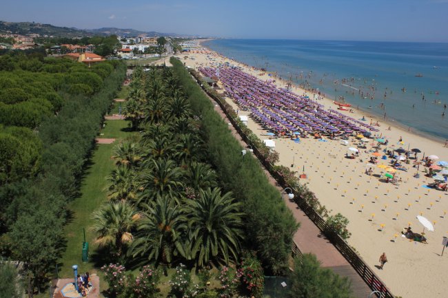 Spiaggia affollata con ombrelloni viola, vista dall'alto.