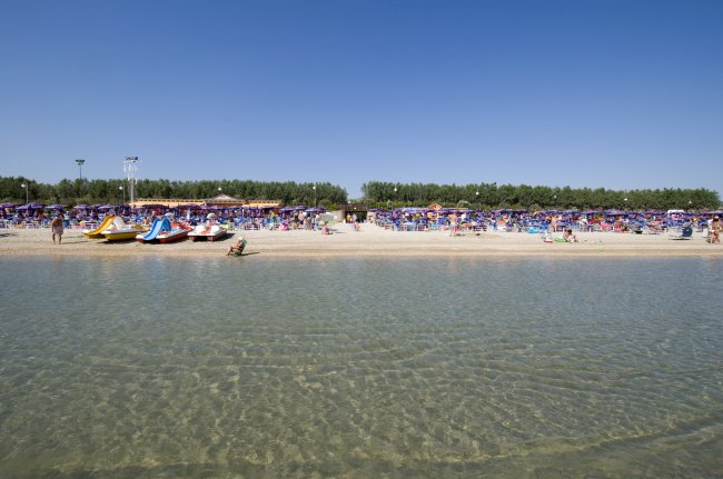 Una spiaggia affollata con pedalò sulla riva.
