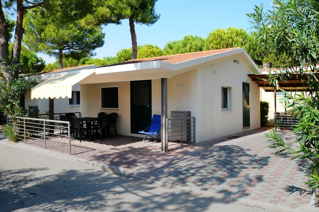 Bungalow bianco con terrazza e tenda gialla.
