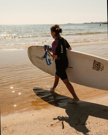 Persona con tavola da surf cammina verso il mare.