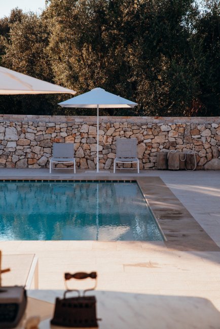 Piscina con sedie e ombrelloni vicino a muro di pietra.