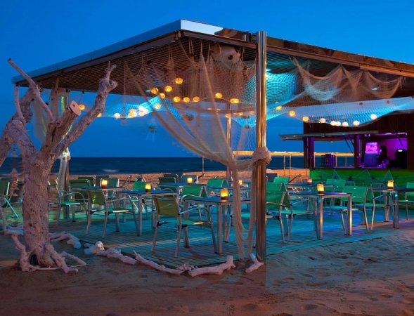 Bar sulla spiaggia illuminato di sera, con sedie verdi.