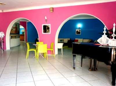 Interno colorato con pareti rosa e blu, tavolini gialli e un pianoforte nero.