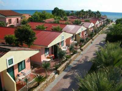 Case con tetti rossi lungo un viale alberato, vicino al mare.