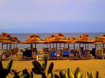 Spiaggia con ombrelloni di paglia, lettini e mare sullo sfondo.
