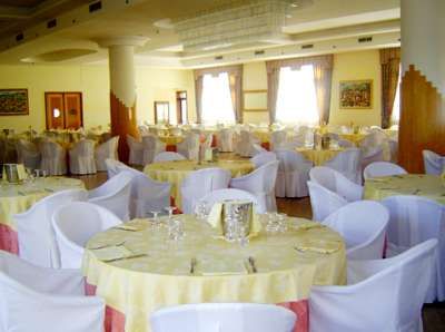 Tavoli rotondi apparecchiati in una sala banchetti elegante con sedie coperte da fodere bianche.