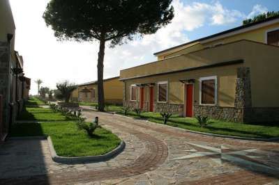 Viale pavimentato tra edifici bassi con tetti inclinati in un'area verde.