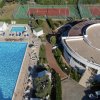 Piscina ampia con sedie a sdraio, accanto a un edificio e campi da tennis.