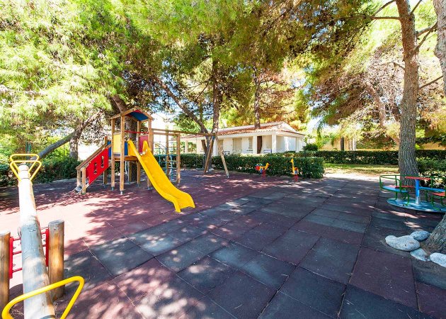 Parco giochi con scivolo e area ombreggiata.