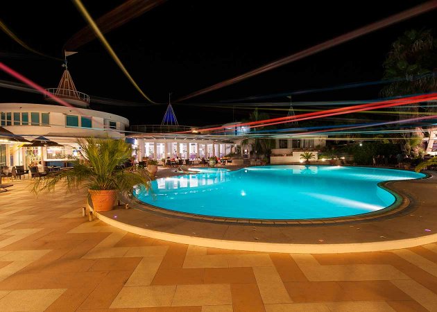 Piscina illuminata di notte con giochi di luce colorati.