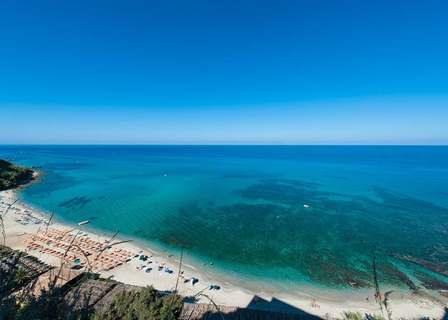 Spiaggia con ombrelloni e mare cristallino visto dall'alto.