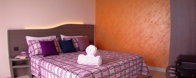 Letto matrimoniale con copriletto rosa e cuscini colorati.