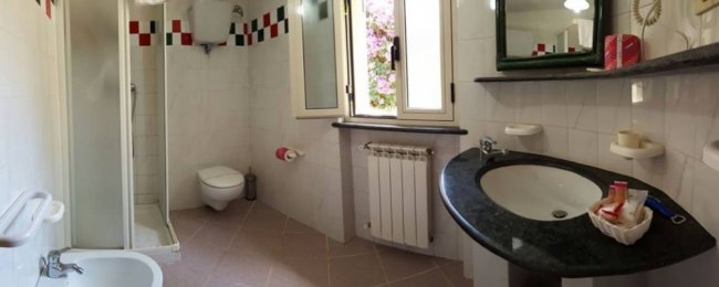 Bagno bianco con doccia, lavandino e finestra.