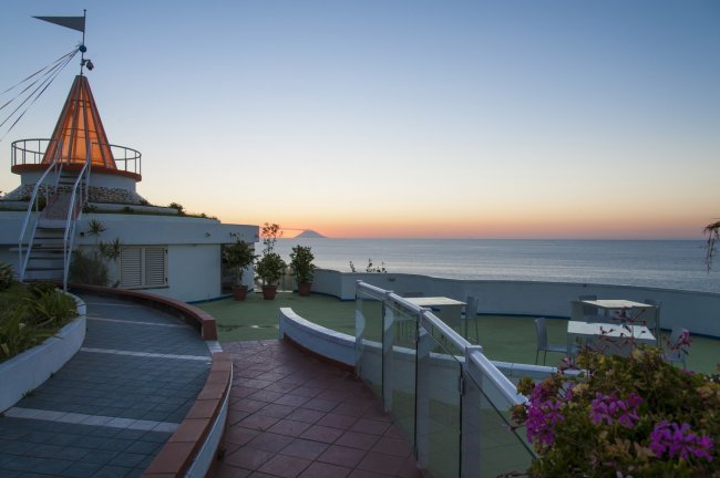 Terrazza con vista mare al tramonto e struttura conico-arancione.