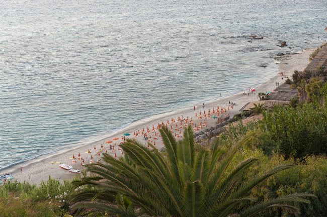 Vista dall'alto di una spiaggia con ombrelloni arancioni e palme.