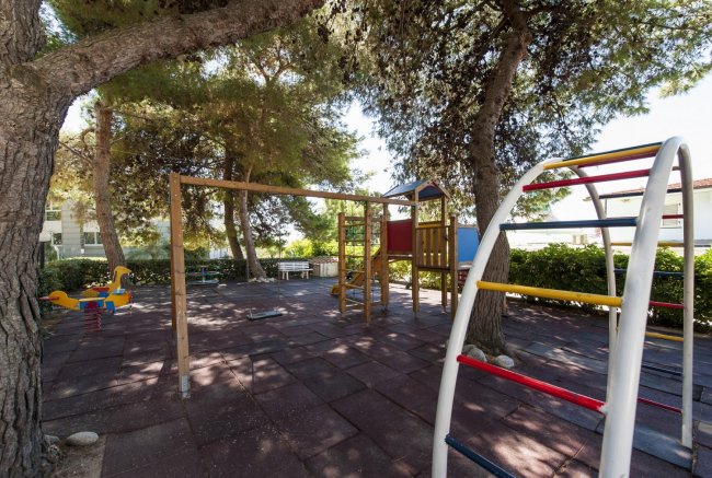 Parco giochi ombreggiato con scivolo e altalena.