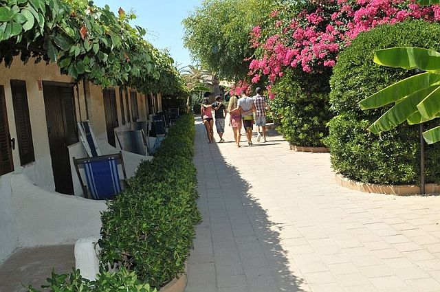 Sentiero tra bungalow e fiori colorati con persone che camminano.