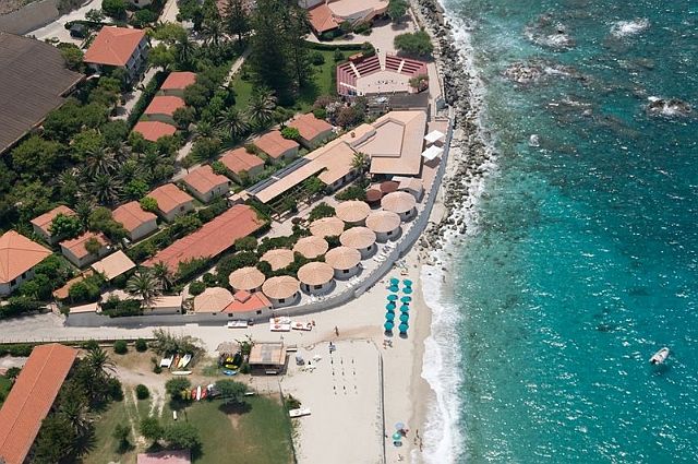 Vista aerea di case accanto a una spiaggia con ombrelloni colorati.