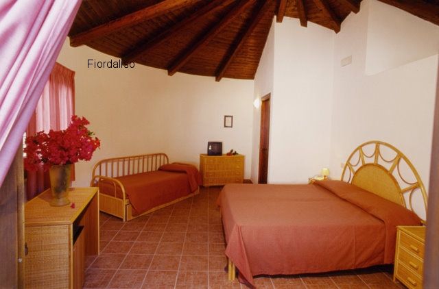 Camera da letto con tetto in legno, due letti e arredamento in vimini.