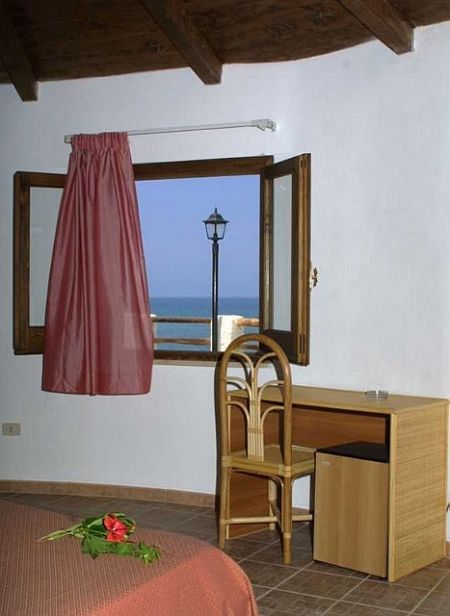 Una stanza con finestra vista mare, tavolo e sedia.