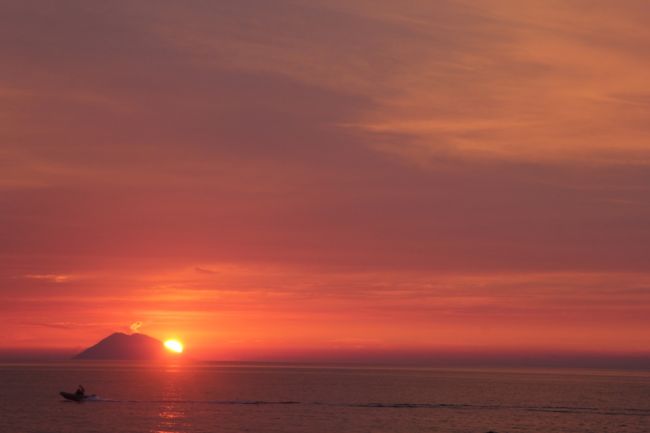 Tramonto rosato sul mare con isola all'orizzonte.