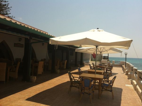 Terrazza con tavoli, sedie e ombrelloni vicino al mare.