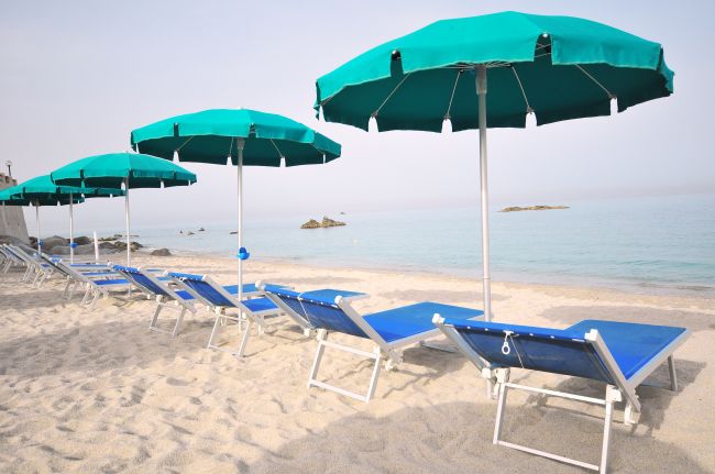 Sedie a sdraio blu e ombrelloni verdi su spiaggia sabbiosa.