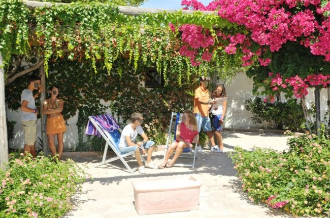 Persone in giardino con sedie a sdraio sotto un pergolato fiorito.