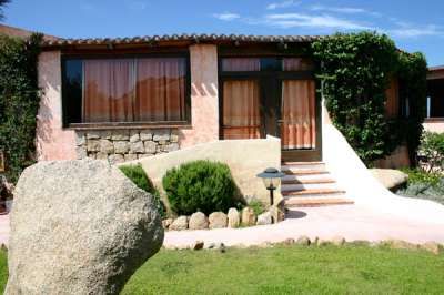 Casa con facciata in pietra, scale e giardino verde, cielo azzurro sopra.