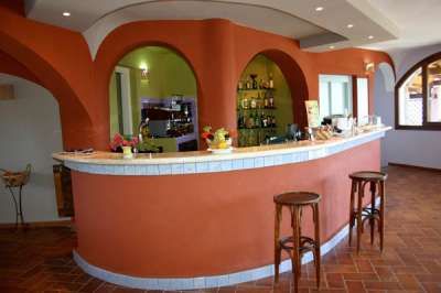 Un bancone di bar curvo color terracotta con sgabelli di legno, decorato con bottiglie e tazze.