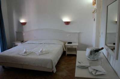 Una camera da letto con letto matrimoniale, luci a muro accese, bottiglia e bicchieri su un tavolo.