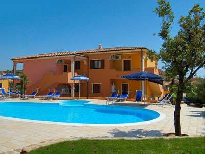 Piscina all'aperto con sdraio blu e ombrelloni, vicino a un edificio arancione.