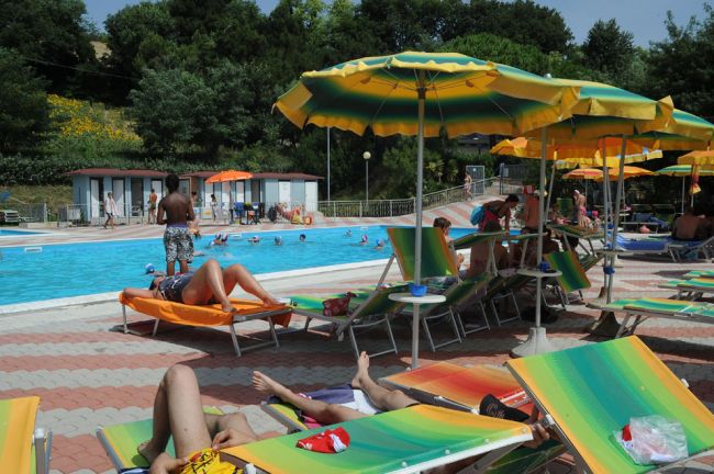 Persone rilassate in piscina con sdraio colorate.